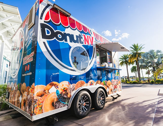 A DonutNV trailer sits outside in the sunshine with palm trees in the background.